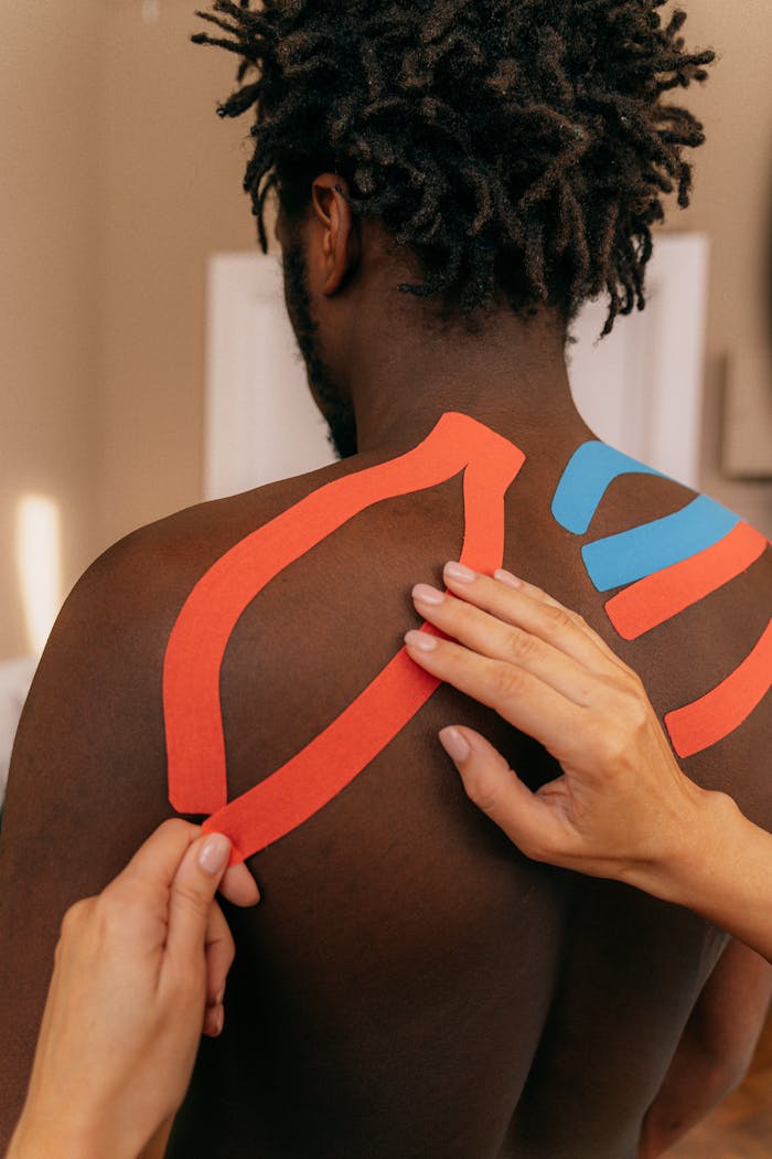 Close up of kinesio tape application on a man's shoulder for pain relief therapy.